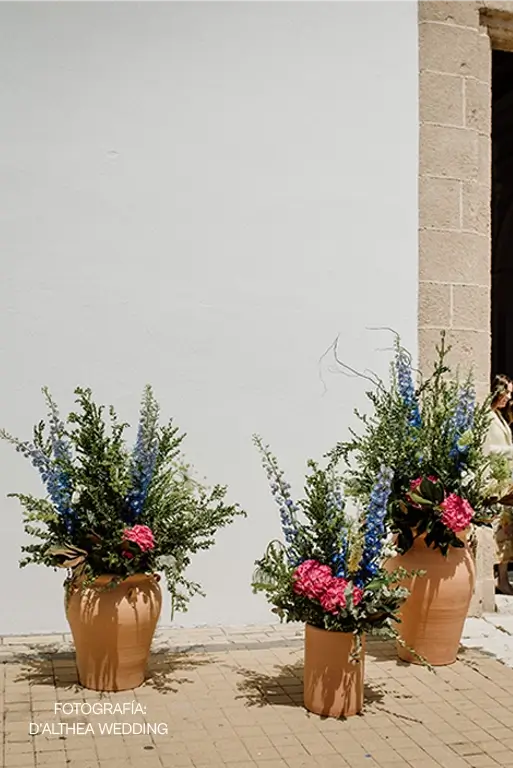Decoración floral para boda civil con jarrones de barro y arreglos de delfinios azules, hortensias fucsias y follaje verde en la entrada del ayuntamiento