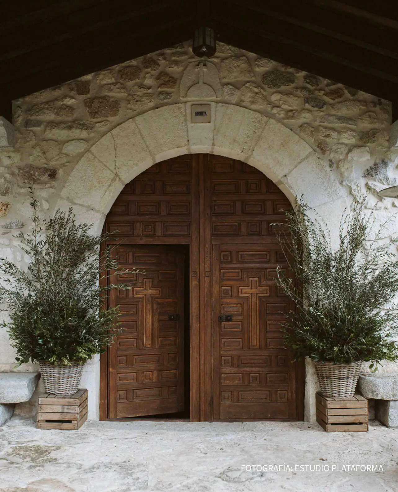 Ambientación floral de boda con ramas verdes en cestas rústicas junto a puerta de iglesia