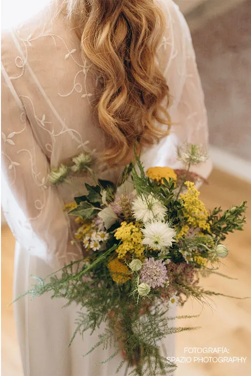 Novia de espaldas con ramo natural en blanco, amarillo y verde para boda religiosa en tonos suaves